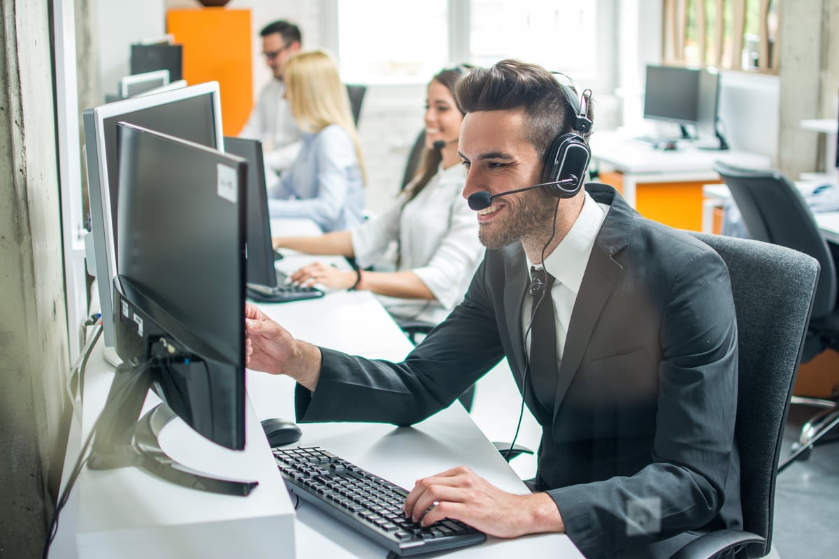 Smiling male customer support operator agent with hands-free device working in call center